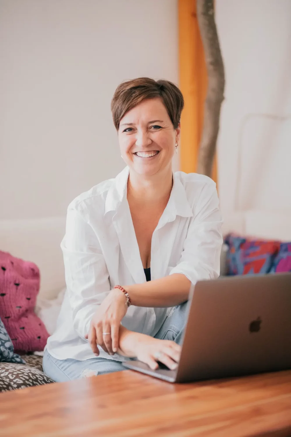 steffi sitzt auf der couch und lacht in die kamera, eine hand am laptop