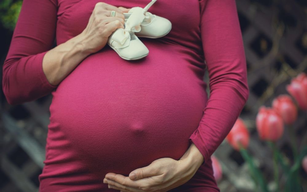 babybauch in himbeerrotem kleid mit weißen babyschuhen